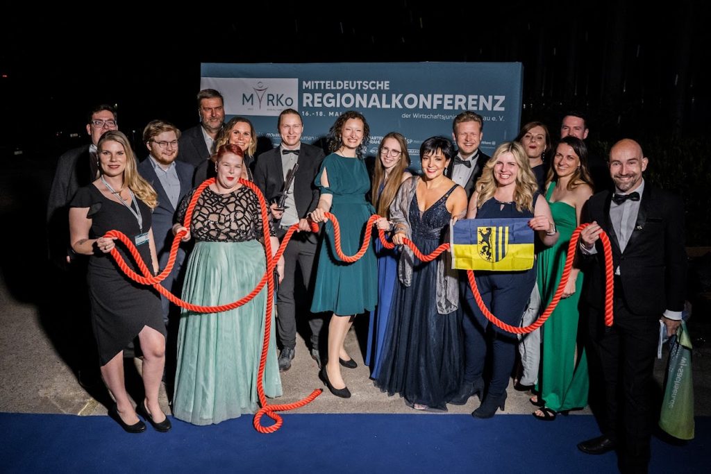Die Mitglieder von WJ Leipzig präsentieren sich in einem Gruppenfoto auf der MiRKo in Dessau in Gala-Kleidung. Alle sind über ein rotes Seil miteinander verbunden.